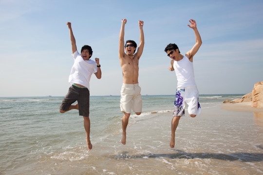 三个休闲装年轻男人在海边跳跃