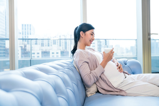 年輕孕婦在沙發(fā)上喝牛奶