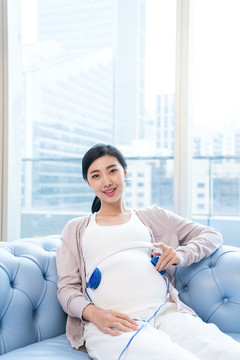 年輕孕婦在沙發(fā)聽(tīng)音樂(lè)