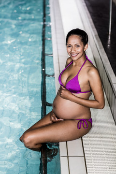 游泳池里微笑着的孕妇摸着肚子