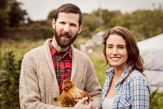 一对微笑的夫妇在乡下牵着一只鸡