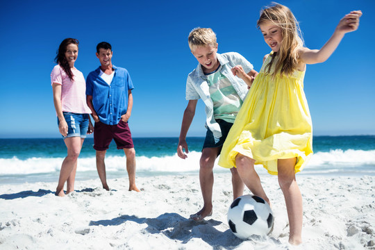 可爱的家庭在海滩上踢足球