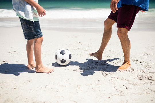 爸爸和儿子在海滩上踢足球