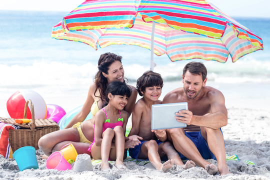 可爱的家庭在沙滩上使用平板电脑