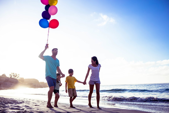 可爱的家庭在海滩上散步和拿气球