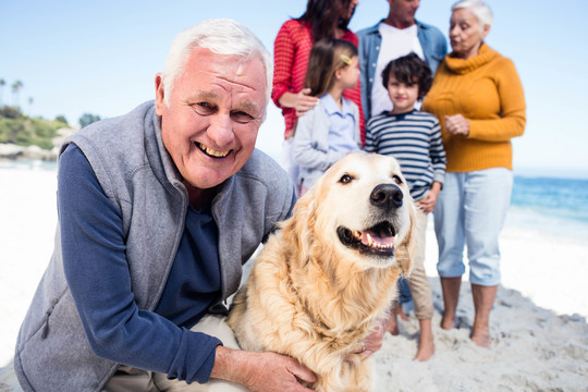 可爱的爷爷抱着狗和家人在海滩上