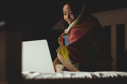 黑发女人裹着毯子看笔记本电脑