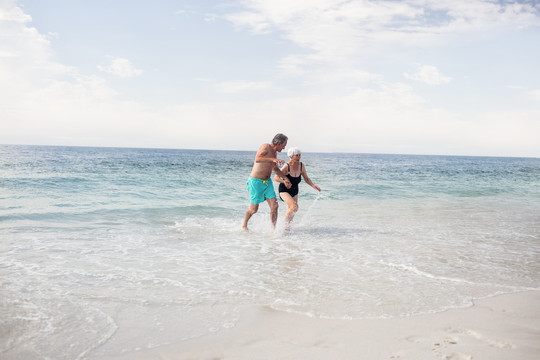 老年夫妇手牵着手在海滩上奔跑