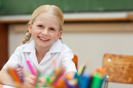 微笑的小学生坐在桌旁用钢笔