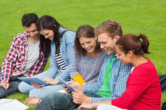 五个学生坐在草地上用平板电脑