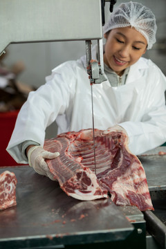 肉厂用带锯机切割生肉的女屠夫