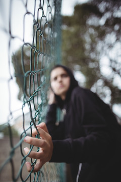焦急的女孩倚在校园铁丝网围栏上