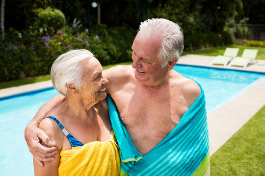 在游泳池边裹着毛巾的老年夫妇