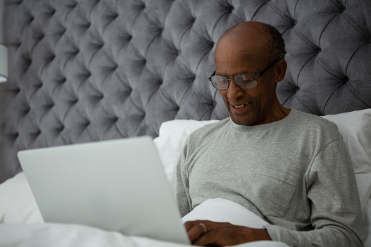老人在家里床上用笔记本电脑