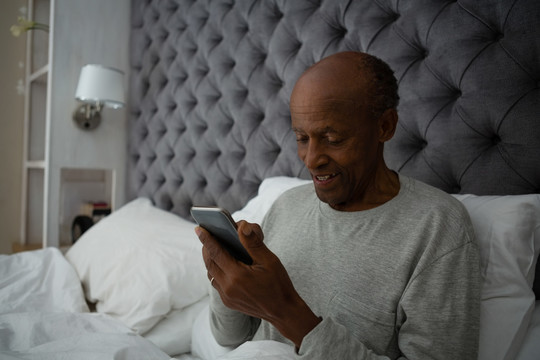 老人坐在床上用手机