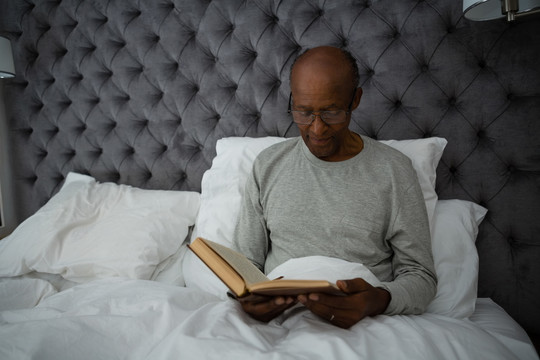 老人坐在床上看书