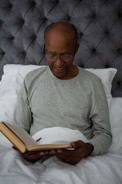 微笑的老人坐在床上看书