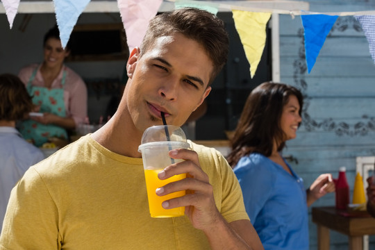 年轻人站在食品车旁喝果汁