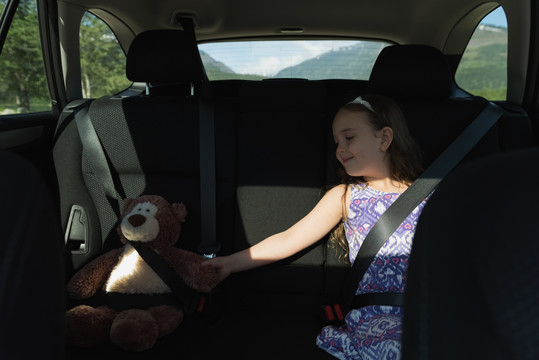 坐在汽车后座上的泰迪熊和小女孩
