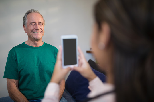 女治疗师用手机拍摄老年男性患者