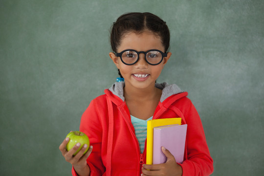 戴眼镜的小女孩拿着苹果和书