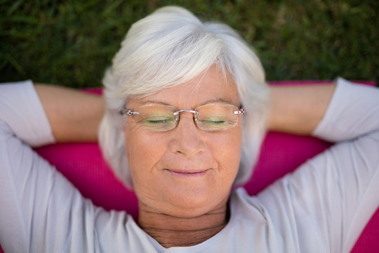 闭着眼睛躺在运动垫上的老年妇女