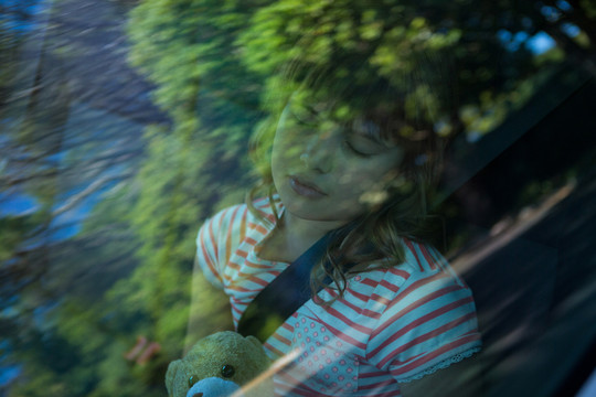 小女孩和泰迪熊睡在汽车后座上