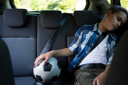 十几岁的男孩坐在车里踢足球