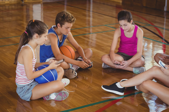 高中队坐在篮球场上用手机