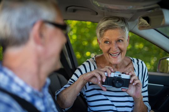 开朗的老年妇女在车里给男人拍照
