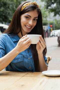 坐在路边咖啡馆喝咖啡的微笑女人
