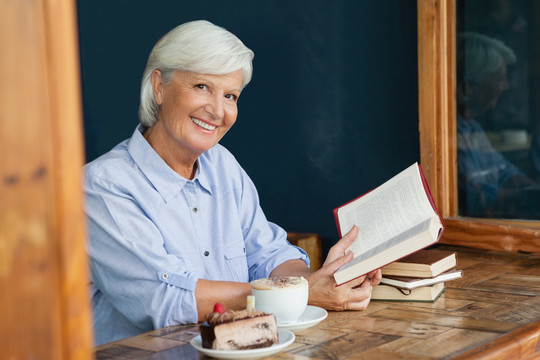坐在咖啡馆里拿着书微笑的老妇人