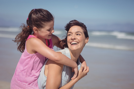 快乐的母亲在海滩上背着女儿
