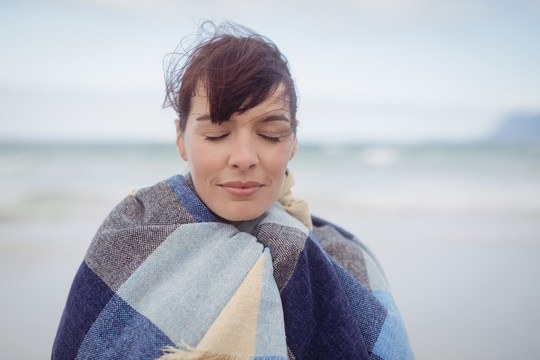 在海滩上裹着毯子的年轻女子