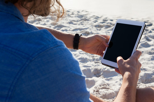 在海滩上使用平板电脑的男子