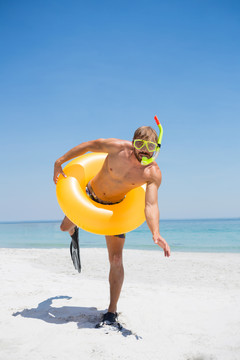 穿着泳圈的顽皮男人在沙滩上跳跃
