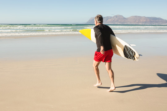背着冲浪板站在沙滩上的男子