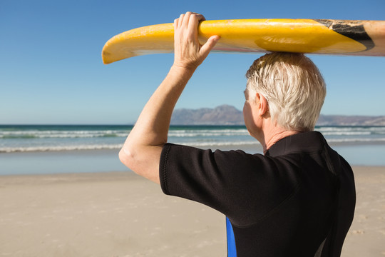 在海滩上扛着冲浪板的老人