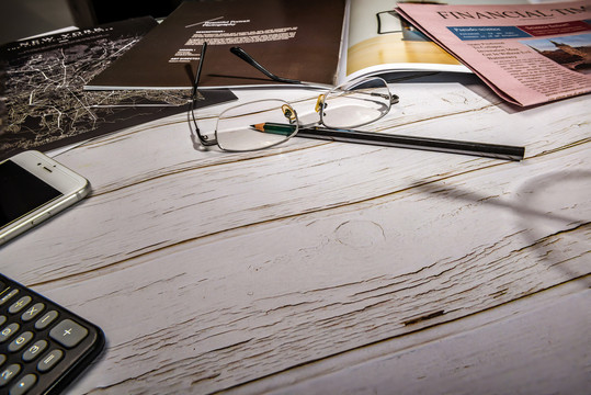 白色木纹桌面上的眼镜铅笔手机