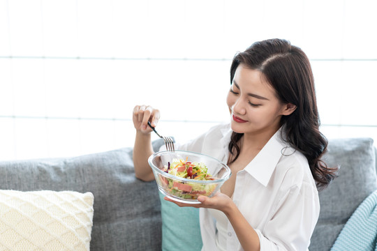 年轻女子坐在沙发上吃色拉