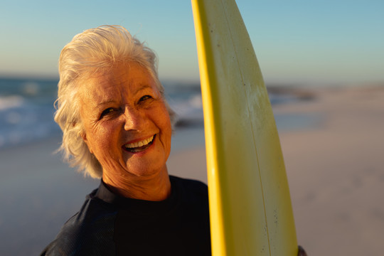 在海边拿着冲浪板的老太太