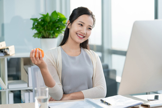 年轻女子在办公室拿着一个橙子