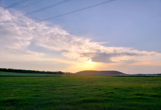 碧绿草原山丘上的落日和晚霞