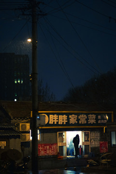 路灯下有人走出雨中的小饭馆