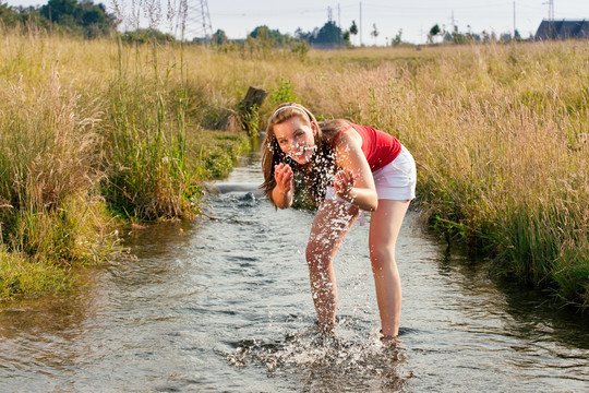 女人站在一条小溪里，脚踝浸在水里，凉水在夏日的炎热中沁人心脾