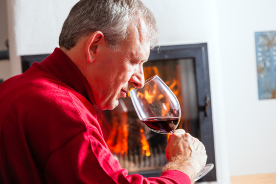 成熟的男人在壁炉前喝一杯红酒