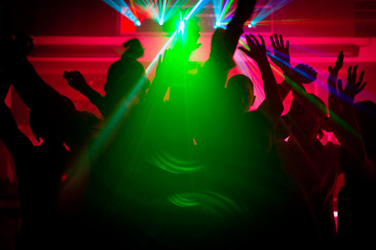 跳舞的人们在迪斯科俱乐部举行庆祝活动的剪影，灯光秀通过背光发射激光束