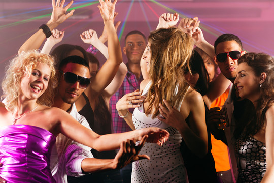 一群不同种族的男女朋友在迪斯科俱乐部里随着音乐跳舞，玩得很开心