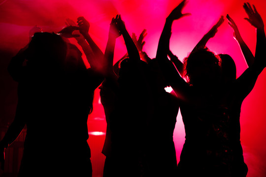 跳舞的人们在迪斯科俱乐部举行庆祝活动的剪影，灯光透过人们的剪影闪耀