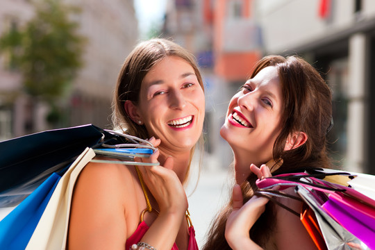 两个女人是朋友，拿着五颜六色的购物袋在市中心购物，她们走在街上玩得很开心